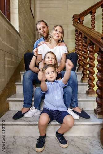 famiglia felice unita in una foto di gruppo nella scala di casa, mentre il piu piccolino gioca a fare il trenino photo