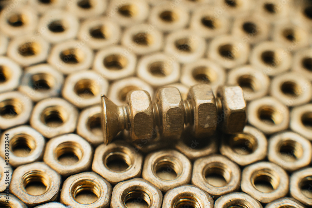 Close-up, macro. Old Soviet brass countersunk head screws with a flat head screwdriver. Texture, background of brass nuts laid out in the form of honeycombs. Gold color screws. Dirty wood screws in oi Close-up, macro. Old Soviet brass countersunk head screws with a flat head screwdriver. Texture, background of brass nuts laid out in the form of honeycombs. Gold color screws. Dirty wood screws in oi