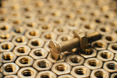 Close-up, macro. Old Soviet brass countersunk head screws with a flat head screwdriver. Texture, background of brass nuts laid out in the form of honeycombs. Gold color screws. Dirty wood screws in oi