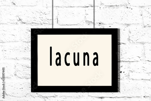 Black frame hanging on white brick wall with inscription lacuna