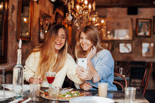 selfie time. funny meeting of two friends after quarantine in a restaurant  girls exchange good news and take selfie on the phone.        