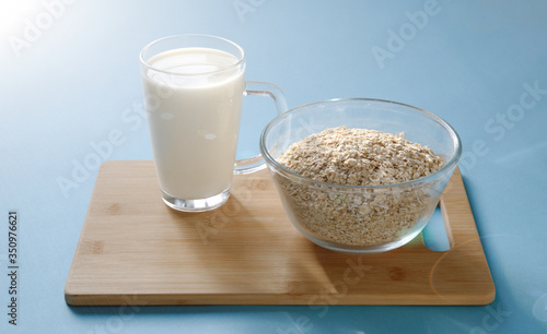 glass of milk and a glass bowl with oatmeal on a wooden board and a blue background
