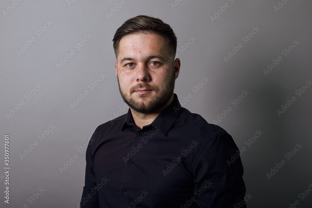 Young Bearded Dark Haired Man In Black Stylish Shirt On Gray Background, Portrait Of Confident, Charismatic Male Looking Straight. Close Up