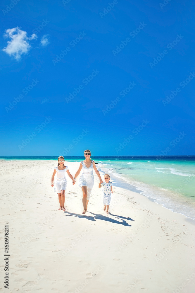 Happy family running on the beach. A mother with her daughter and son enjoying a vacation by the ocean.