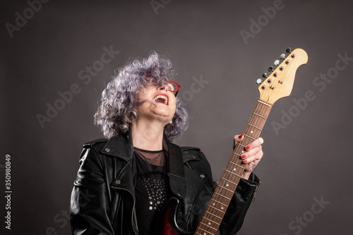 Close up portrait of beautiful old woman playing electric guitar on a gray background