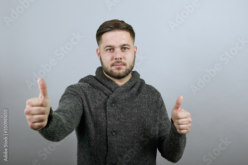 Bilde på lerret Young Bearded Dark Haired Man In Black Stylish Shirt On Gray Background, Serious Male Holds Thumb Finger Up, Looks Straight Ahead