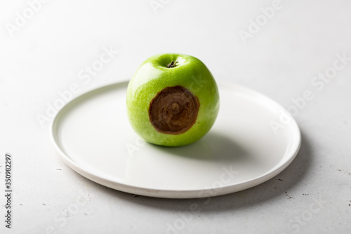 rotten green apple on a plate on a white background.