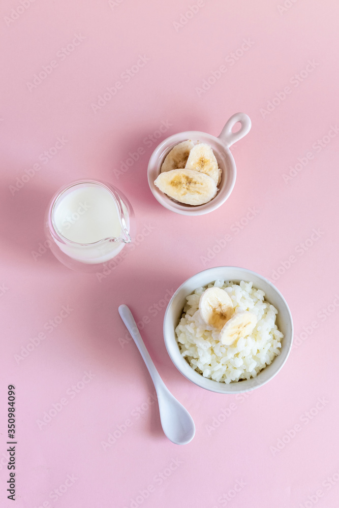 Rice milk porridge with banana slices, daughter and milk on a pink background, top view, flat lay. Vertical Rice milk porridge with banana slices, daughter and milk on a pink background, top view, flat lay. Vertical
