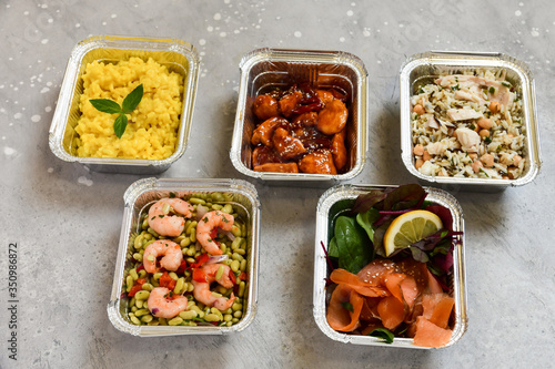 Food delivery. Different aluminium lunch box with healthy natural food risotto, chicken chickpeas and rice, salmon salad, hot chicken teriyaki, shrimp and green beans. airlines food. airline meals