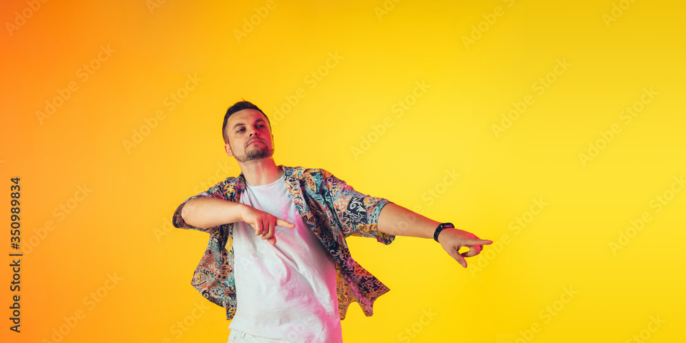 Fototapeta premium Young caucasian musician in casual dancing on gradient yellow background in neon light. Concept of music, hobby, festival. Joyful party host, DJ, stand upper, dancer. Colorful portrait of artist.