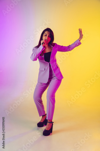 Caucasian female singer portrait isolated on gradient studio background in neon light. Beautiful female model in pink wear with microphone. Concept of human emotions, facial expression, ad, music, art © master1305