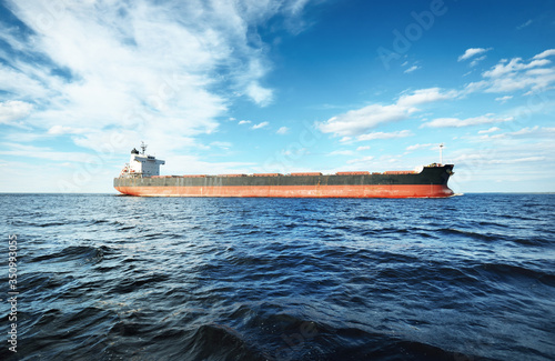 Large bulk carrier (cargo ship) sailing in an open sea from Europoort. Clear blue sky with cirrus clouds. Rotterdam, Netherlands. Global communications, logistics, industry theme