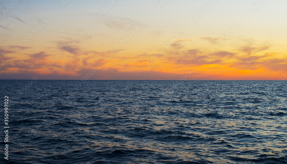 Bright yellow-orange clouds frozen along the horizon above the dark blue surface of the sea.