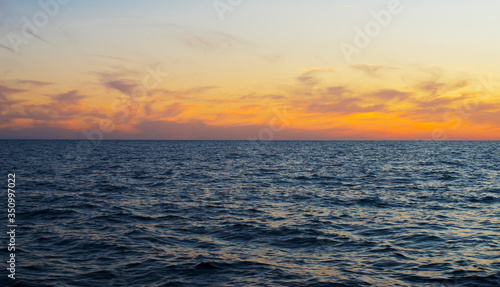 Bright yellow-orange clouds frozen along the horizon above the dark blue surface of the sea.