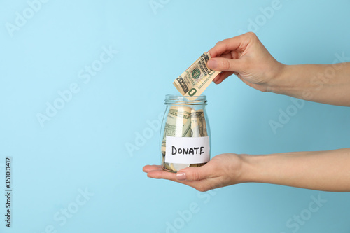 Female hand puts money in glass jar on blue  background