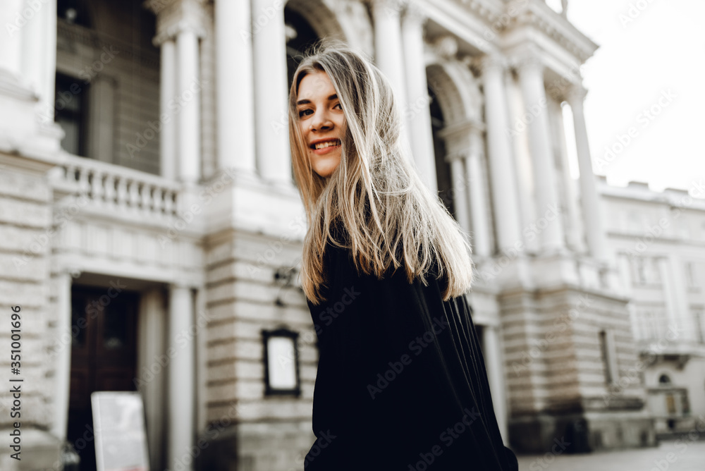 A beautiful young woman in a black dress with blond hair walks around the city with a bag with red flowers A beautiful young woman in a black dress with blond hair walks around the city with a bag with red flowers