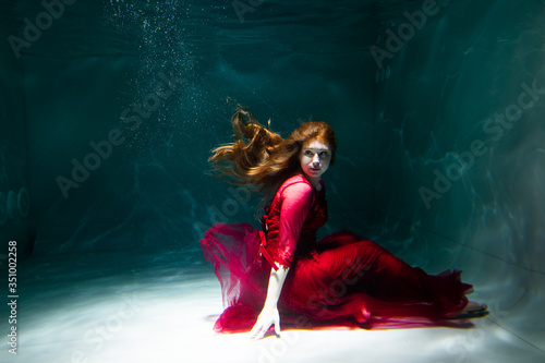 Beautiful girl underwater in a red dress swims in the pool. Tenderness and elegance. Bubbles and a lot of water