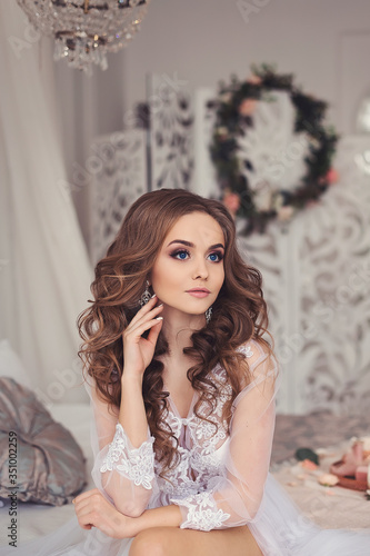 Portrait of a beautiful young girl with natural makeup in a white transparent boudoir dress. Preparing for the wedding, bride's morning. © Anna