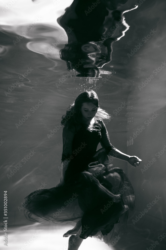 Obraz premium Black and white photo. Beautiful girl underwater in a red dress swims in the pool. Tenderness and elegance. Bubbles and a lot of water