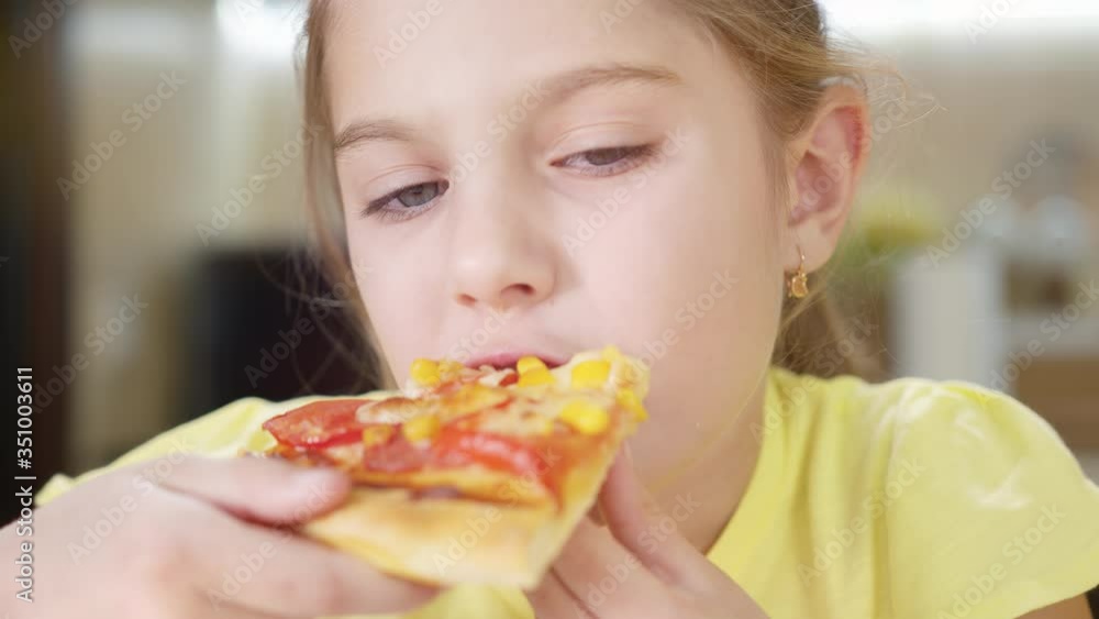 Little girl bites a slice of pizza close up and deliciously eats pizza. The girl appetizingly chews pizza. Little girl bites a slice of pizza close up and deliciously eats pizza. The girl appetizingly chews pizza.