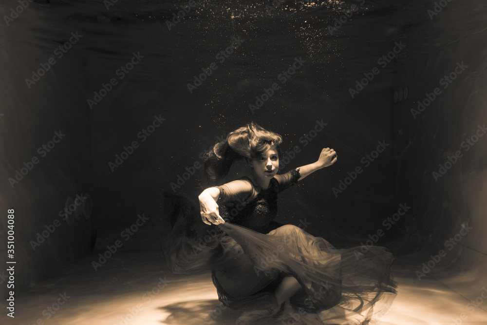 Black and white photo. Beautiful girl underwater in a red dress swims in the pool. Tenderness and elegance. Bubbles and a lot of water