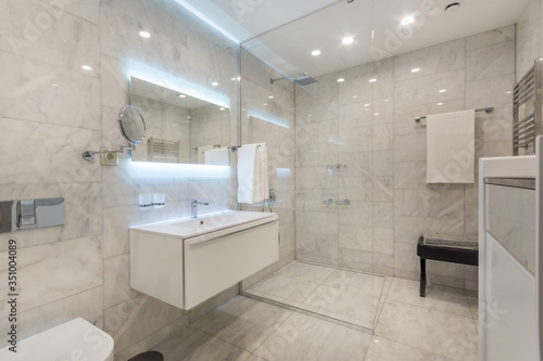 Beautiful modern bathroom with large backlit illuminated mirror  sink  and glass shower