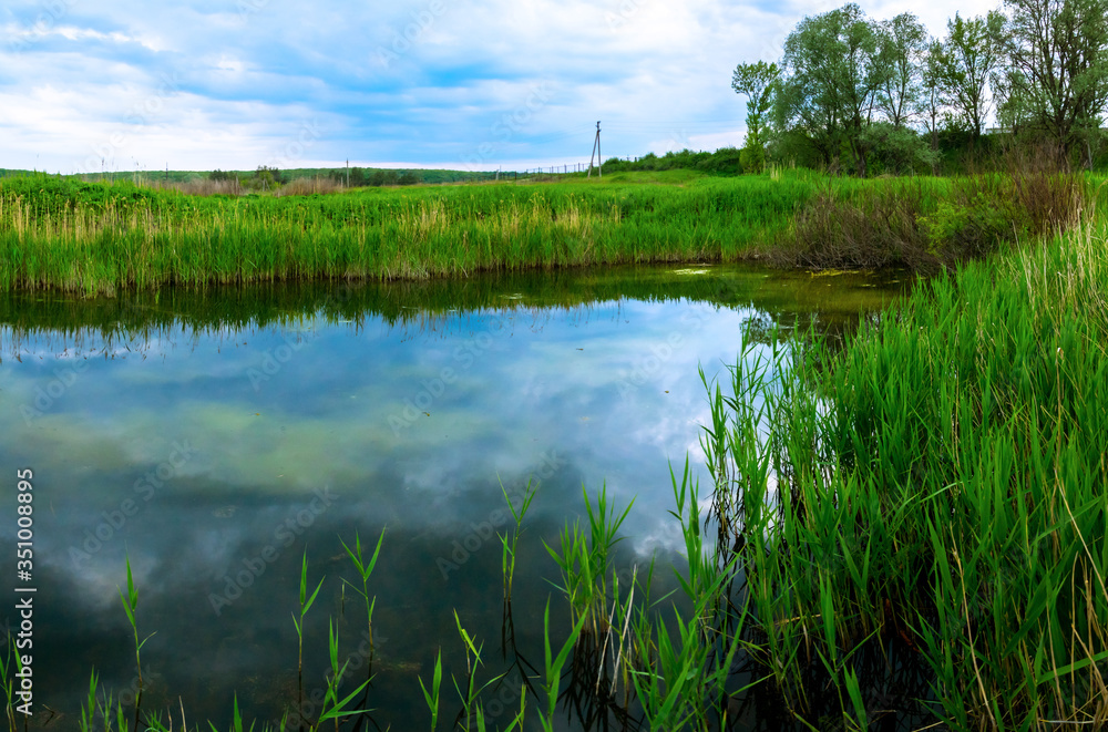 Landscape of a small pond during a cloudy sunset, panorama of the nature of the country Landscape of a small pond during a cloudy sunset, panorama of the nature of the country