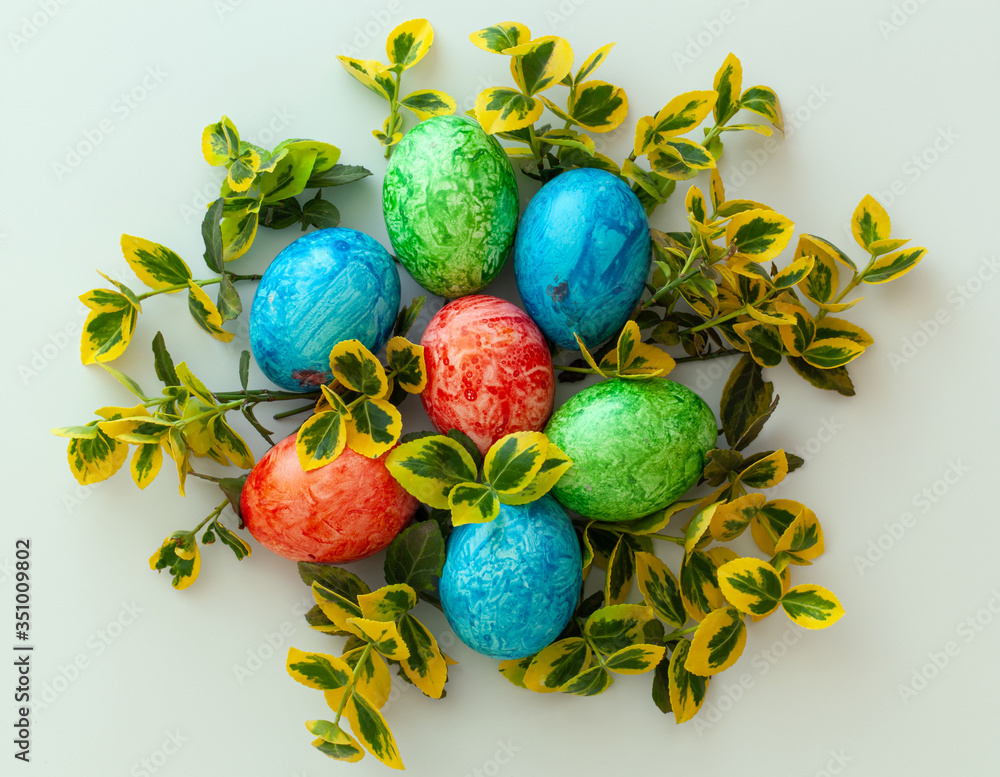 Colorful Easter holiday eggs, arranged with green twigs and an orange wreath of grass on a white background.