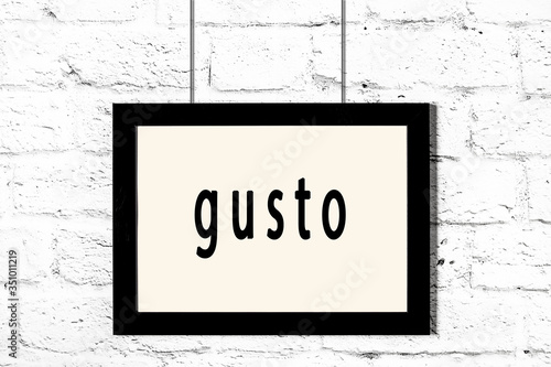 Black frame hanging on white brick wall with inscription gusto