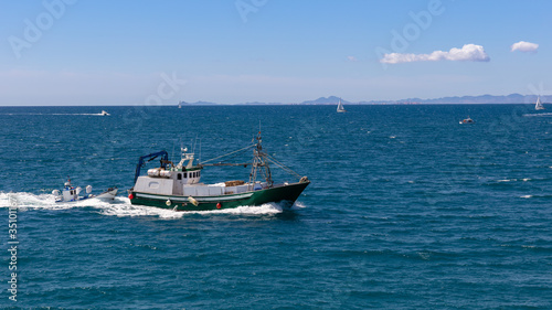 A fishing trawler returns from fishing to the port of the Spanish city of Torrevieja. There are also sailing boats on the Mediterranean. Mountains can be seen in the background in the south. © wewi-creative