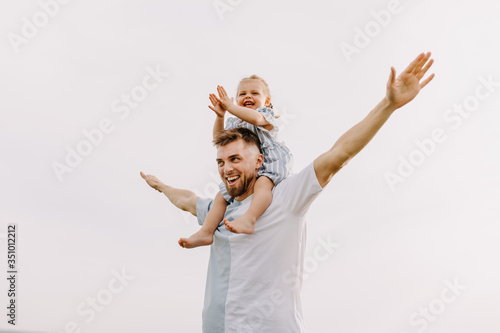 Young man and little girl playing in an open field, outdoors. Daughter sitting on father's shoulders, on white clean background.