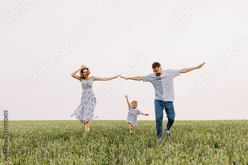 Woman, man and a little girl running on a wheat green field. Happy family on summer day, playing outdoors. Concept of aviation.