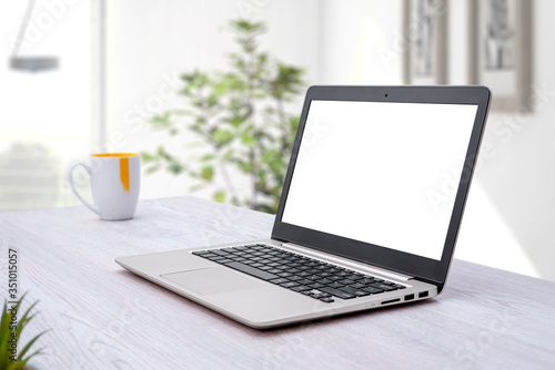 Laptop computer mockup. Home work desk with coffee mug beside. Plant in background