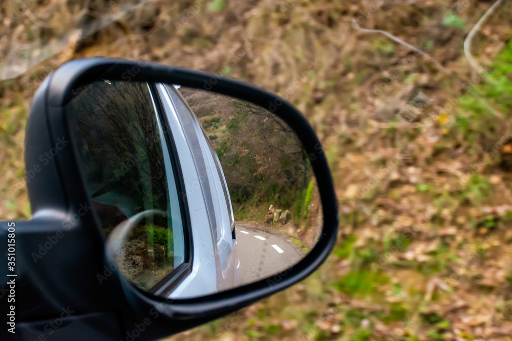 A close-up shot of the reflection of a white van in the rearview mirror of a moving car