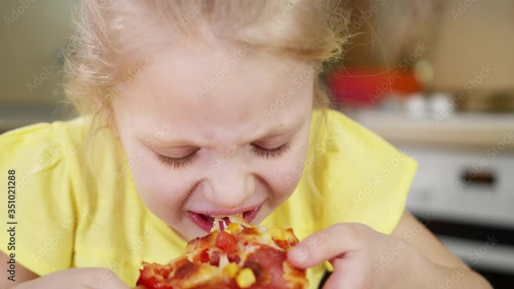 Little girl bites a slice of pizza close up and deliciously eats pizza. The girl appetizingly chews pizza. Little girl bites a slice of pizza close up and deliciously eats pizza. The girl appetizingly chews pizza.