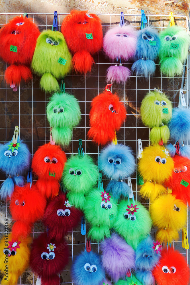 Multicolored fluffy keychains with eyes hanging on a grid outdoors