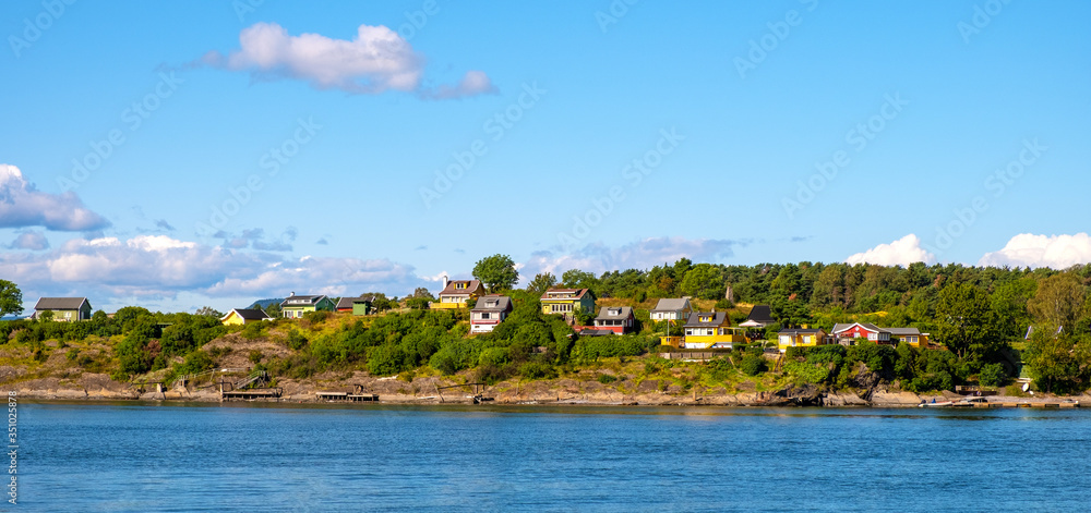 Panoramic view of Lindoya island on Oslofjord harbor near Oslo, Norway, with summer cabin houses at wooded shoreline in early autumn