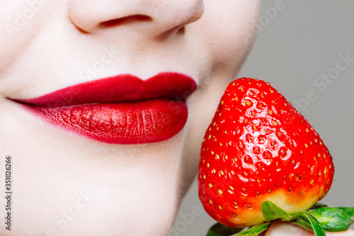 Macro close up of caucasus woman's lips with red lipstick and fresh strawberry.