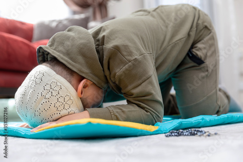 Little boy wearing green clothes and wearing a fez is praying.