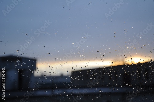 Drops of rain on glass against the background of an industrial landscape, rain sky and a line of sunset light