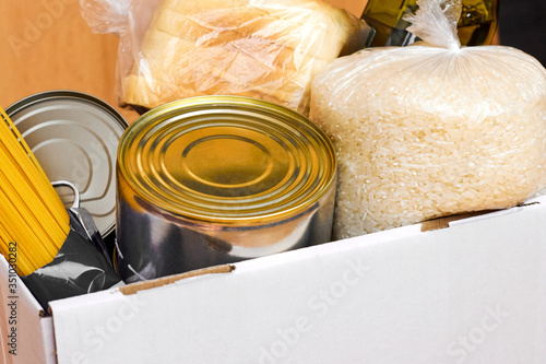 Donation box with canned food, pasta and rice on a wooden background. Food delivery or charity concept