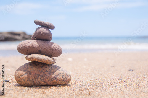 Five stones balanced on the sand close to the ocean at the beach.