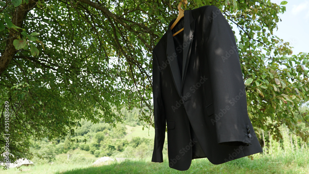 Close-up photo of groom's jacket hanging on the tree branch outdoors. Wedding day Close-up photo of groom's jacket hanging on the tree branch outdoors. Wedding day