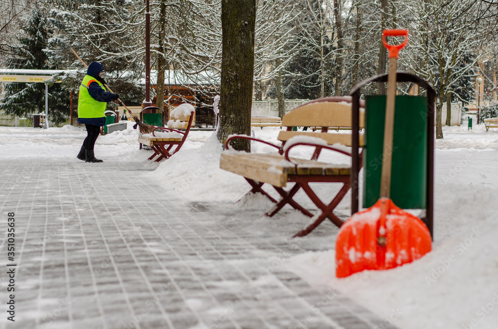 Naklejka premium snow storm in the city. Roads and sidewalks covered with snow. Worker shovel clears snow. Bad winter weather. Street cleaning after snowstorm.