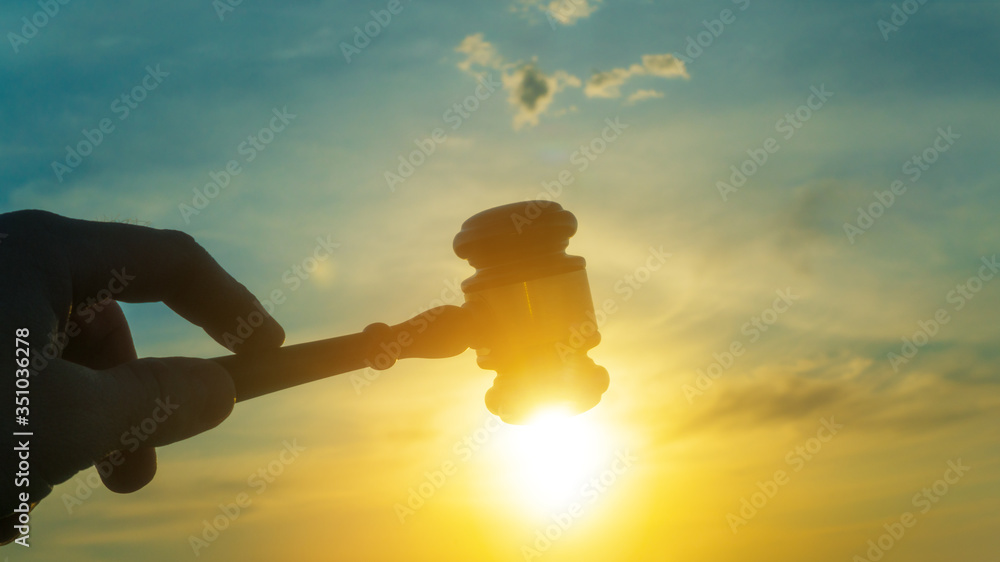 Gavel in the hand of a judge on sunset sky background. Verdict, court, crime and punishment