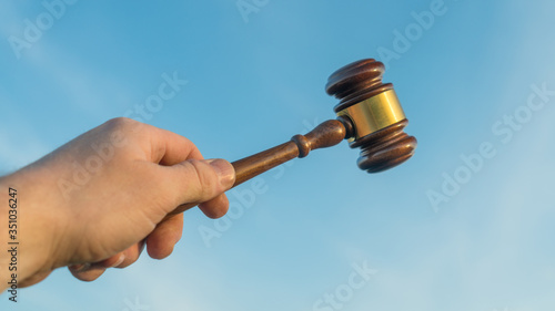 Gavel in the hand of a judge against a blue sky. Verdict, court, crime and punishment