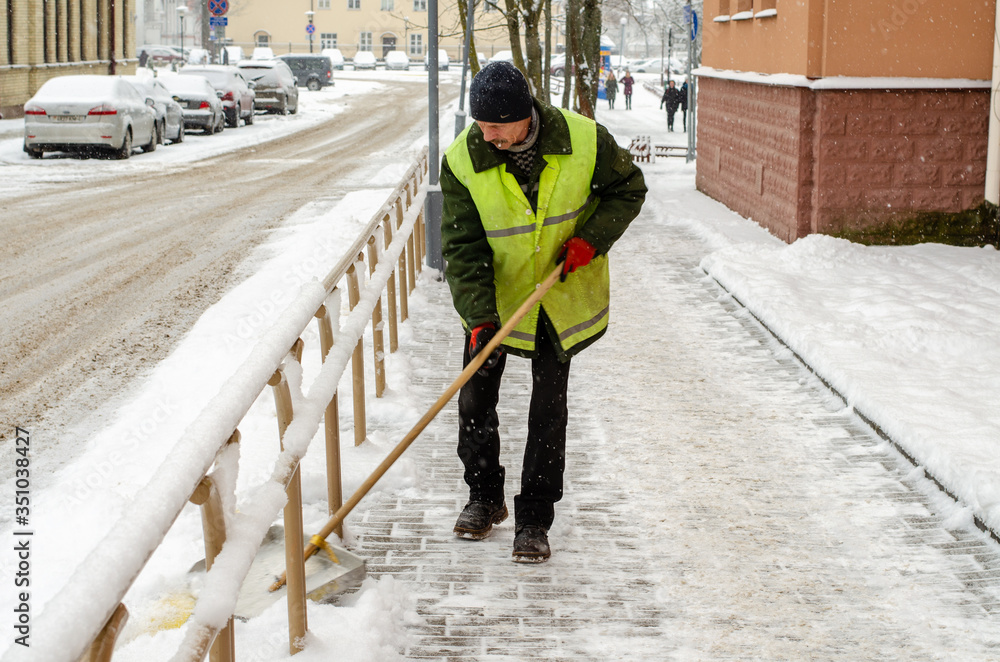 snow storm in the city. Roads and sidewalks covered with snow. Worker shovel clears snow. Bad winter weather. Street cleaning after snowstorm.