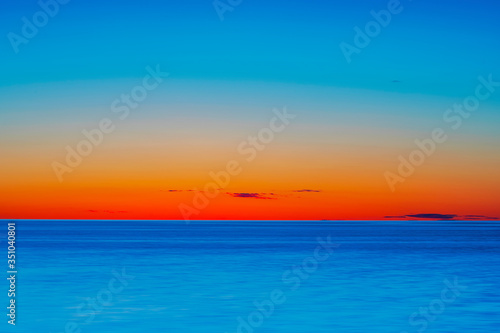 Vibrant colored summer sunset reflecting in ocean with endless horizon and deep blue ocean at island of Gotland in Sweden