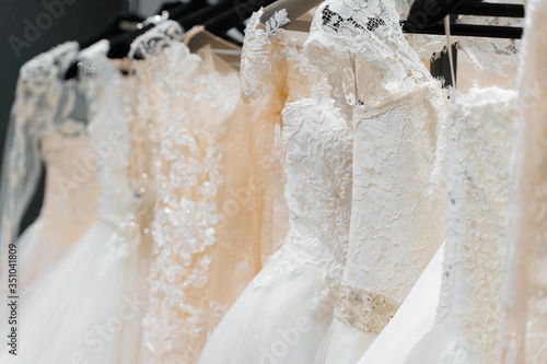 Wedding dresses made of silk chiffon, tulle and lace. Beautiful White cream bridal dress on hangers in wedding salon. Pearls and crystals pendants on the sleeves of a delicate color of a wedding dress