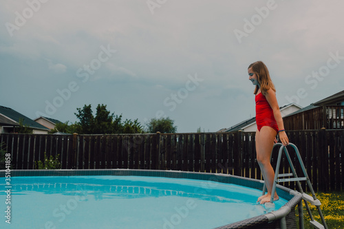 chica joven divirtiéndose bebiendo un vaso de limonada en la piscina en un día caluroso de verano con gafas de sol en bañador rojo